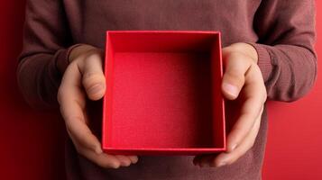 A pair of hands presents an open red box, suggesting a delivery parcel just received. The box is empty, contrasting with the solid red background, emphasizing anticipation and mystery. photo