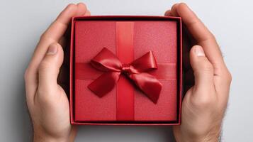 A pair of hands holds a carefully wrapped red box with a matching ribbon. This moment captures the excitement of receiving a parcel, symbolizing a thoughtful gift. photo