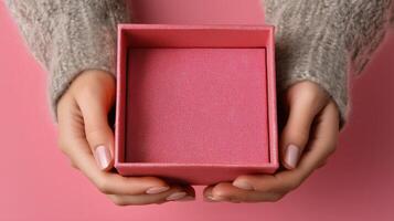 A pair of hands gently holds an open pink box against a soft pink background. The box appears empty and ready for a special delivery or a thoughtful gift. Warm, cozy textures highlight the scene. photo