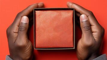 Two hands gently grasp an open box, showcasing its textured exterior. The box rests on a vivid red surface, highlighting its warm color. This moment captures the anticipation of discovery. photo