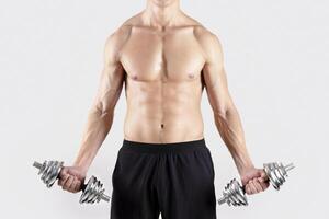 Full length portrait of motivated millennial bodybuilder exercising with dumbbells over light studio background. Focused young sportsman with naked torso pumping up iron, working out with weights photo