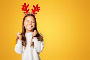 Feels euphoric. Happy little girl in sweater, with horns, closed eyes, isolated on yellow background, studio shoot photo