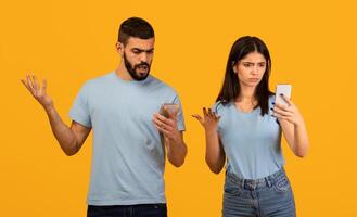 No WiFi. Disappointed middle eastern spouses with smartphones suffering problems with internet or network connection, standing over yellow background, studio shot photo