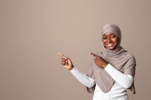 Look There. Positive black muslim lady in hijab pointing with two hands at copy space, smiling religious african woman in headscarf demonstrating free space for your design or advertisement, panorama photo