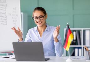 E-learning with teacher, social distancing, new normal. Happy female tutor giving German language lesson online, using laptop. Young lecturer explaining grammar rules to students on internet photo