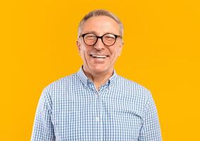 Portrait of senior male smiling wearing glasses and casual checkered shirt posing standing isolated over yellow orange studio background. Happy excited adult person looking at camera, free copy space photo