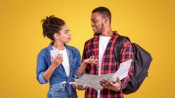 Black Couple Having Quarrel Planning Vacation Holding Smartphone And Tourist Map Choosing Journey Destination Standing On Yellow Studio Background. Travel Navigation Problems Concept photo