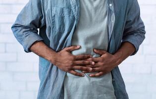 Unrecognizable Black Guy Touching Aching Abdomen Having Painful Stomachache Standing Over Gray Studio Background. African Man Suffering From Stomach Inflammation. Gastritis And Abdomen Pain. Cropped photo