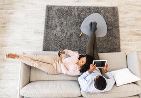 Weekend Leisure. Top Overhead View From Above Of Millennial Black Couple Sitting And Resting On Sofa. Boyfriend Using Digital Tablet, Girlfriend Chatting On Mobile Phone, Browsing Internet Together photo