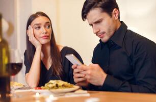 Bad Date. Unhappy Sad Beautiful Woman Is Getting Bored Sitting On Date Event In Restaurant While Her Boyfriend Using Mobile Phone And Chatting, Ignoring His Girlfriend. Relationship Problem Concept photo