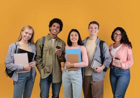 Modern students from different countries and exchange program. Smiling young international people with cups of takeaway coffee, books and backpacks look at camera, isolated on orange background photo
