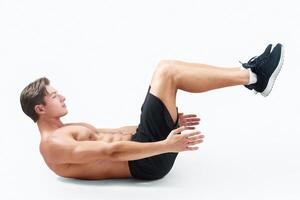 Side view of strong shirtless guy doing abs exercises, training his core muscles on light studio background. Handsome millennial athlete working out with bare chest, full length portrait photo
