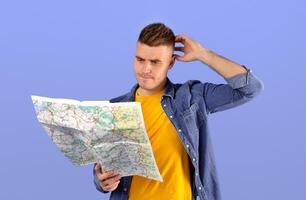 Frustrated young man examining map and scratching head, feeling lost, having problem finding his destination, blue studio background. Travel navigation problems concept photo