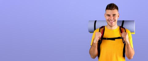Cheerful young guy with tourist gears gesturing YES over blue studio background. Positive millennial hiker thrilled about his journey, anticipating camping trip or adventure photo