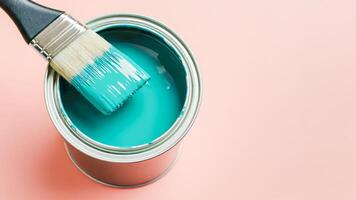 Paintbrush dipped in turquoise paint on open can on pink background with copy space. Perfect for interior design, DIY projects, color trends, painting services and home renovation branding photo