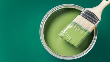 Paintbrush dipped in green paint on open can, creating smooth monochrome composition. Perfect for interior design, DIY projects, color trends, painting services and home renovation branding photo