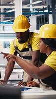 Vertical All black team of engineers comparing solar panels designs on devices, working on the production line at the manufacturing plant. Troubleshooting together and ensuring optimization. Camera B. video