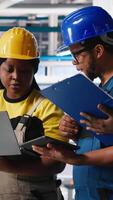 Vertical Technicians group in photovoltaics factory use tracking software on devices, troubleshooting for seamless production line. Black team reviews robot arms manufacturing solar panels. Camera A. video