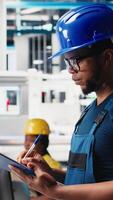 Vertical Black photovoltaics factory technician looking over paperwork documents, analyzing data for production. Solar panels manufacturing plant worker reading files to troubleshoot errors. Camera B. video