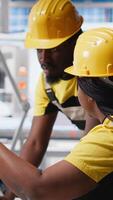 Vertical All black team of engineers comparing solar panels designs on devices, working on the production line at the manufacturing plant. Troubleshooting together and ensuring optimization. Camera A. video
