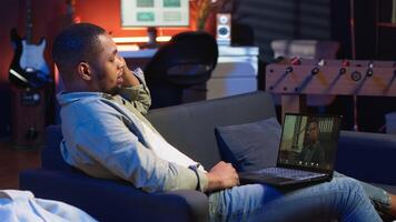 Focused black guy smiling and waving during a web conference in his living room, showcasing online discussion in a digital and wireless lifestyle. Conference speaker with attendees on call. Camera A. video