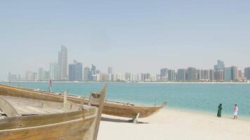 Romantic scene of a couple walking or relaxing on a beach with the stunning modern skyline of Abu Dhabi in the background. A blend of fun, cityscape, and coastal beauty in the UAE. video