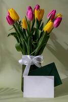 Empty white envelope mock up template Multicolored fresh tulips in vase in green background with trendy deep shadows. Spring flowers in yellow and violet colors. Postcard wallpaper design Copy space photo