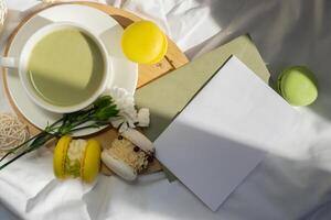 Copy space letter mock up empty envelope Nutrient-rich matcha drink with trendy macaron dessert on wooden tray in bed with fresh flowers. Morning beautiful breakfast present gift idea. Vibrant creative colors. Natural energy givers tea photo