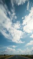 open road under a vast blue sky with fluffy white clouds. The road stretches into the distance, inviting a sense of adventure and freedom. photo