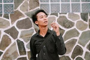 Young man with cigarette against a textured stone wall backdrop photo