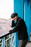 Smiling young man leaning on a blue railing, urban outdoor setting photo
