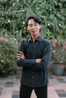 Contemplative young man in garden setting with arms crossed casually photo