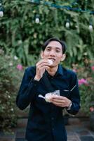 Man enjoying indonesian snack with lush greenery background and soft lighting photo