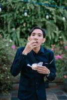 Man in a lush garden snacking on a treat while wearing a dark shirt photo