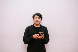 Young man using smartphone against a plain wall in a casual setting photo