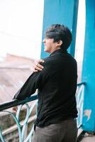 Thoughtful young man smiles on vintage balcony with blue railing photo