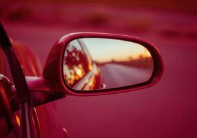 Sunset reflection in dark red cherry car side mirror on scenic road photo