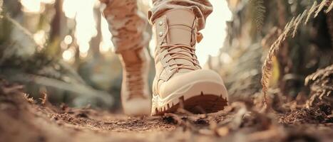 Hiking boots walk on dirt path. Boots on ground in outdoor nature scene. Sunlight shines through foliage in background. Walking on forest trail. photo
