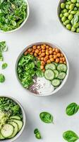 Overhead view of bowls filled with fresh vegetables, beans, chickpeas, and seeds on a light gray background. Healthy, natural and nutritious food photo