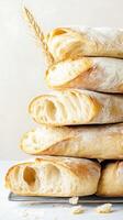 Stack of crusty bread loaves with flour and wheat stalk on light surface. Studio shot of sliced bread showing air pockets photo