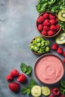 Overhead view of a fresh pink smoothie with raspberries kiwi spinach and mint leaves arranged on a textured gray surface photo