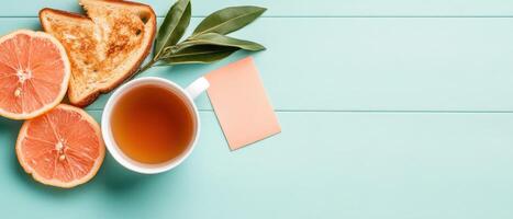 Citrus fruit tea toast and leaves on blue painted wood. Empty card for text. Simple healthy breakfast. Top down view photo