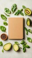 Cookbook with green leaves and avocado halves on light gray table. Ingredients for healthy food. Preparation flat lay with book photo