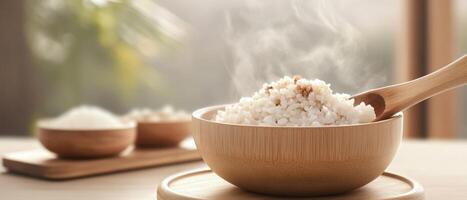 Steaming white rice in bamboo bowl with wooden spoon on table. Simple meal with blurred bowls in background. Healthy warm food concept photo