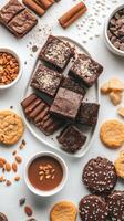 Collection of delicious desserts on white surface. Brownies cookies almonds chocolate chips around a plate and bowl of fudge sauce photo