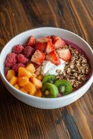 Bowl of fresh fruit and granola. Vegetarian desserts with strawberries, raspberries, kiwi, mango, and yogurt on a wooden table photo