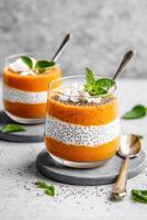 Desserts displayed in clear glass cups. Vegetarian pudding with seeds and orange layer. Coconut and mint topping. Delicious vegan desserts photo