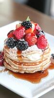 Stack pancakes with fresh berries drizzled syrup and cream filling on white square plate. Sweet vegetarian desserts photo