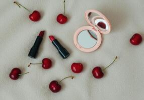 Elegant makeup and fresh cherry still life with lipsticks and compact mirror on textured fabric photo