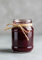 Glass jar filled with homemade cherry preserves tied with a natural linen string. photo